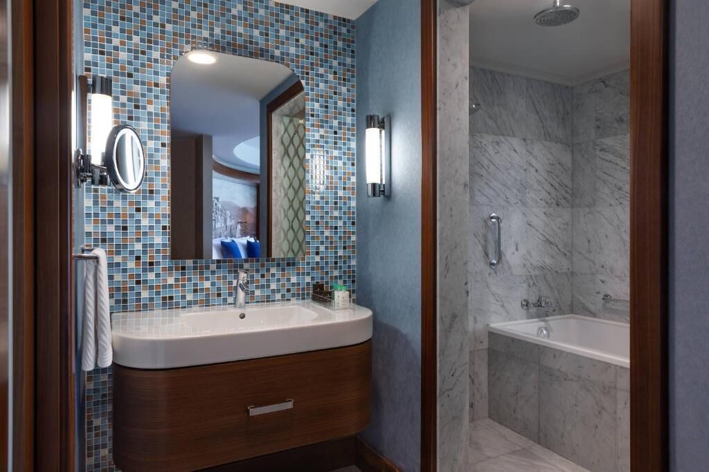 Un baño con pared de mosaicos, tocador de madera, espejo, lavabo, ducha y bañera.