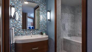 Un baño con pared de mosaicos, tocador de madera, espejo, lavabo, ducha y bañera.