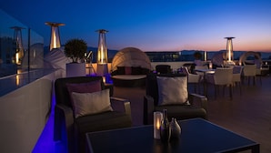 A rooftop lounge area with modern seating, ambient lighting, and a view of the city skyline at dusk.