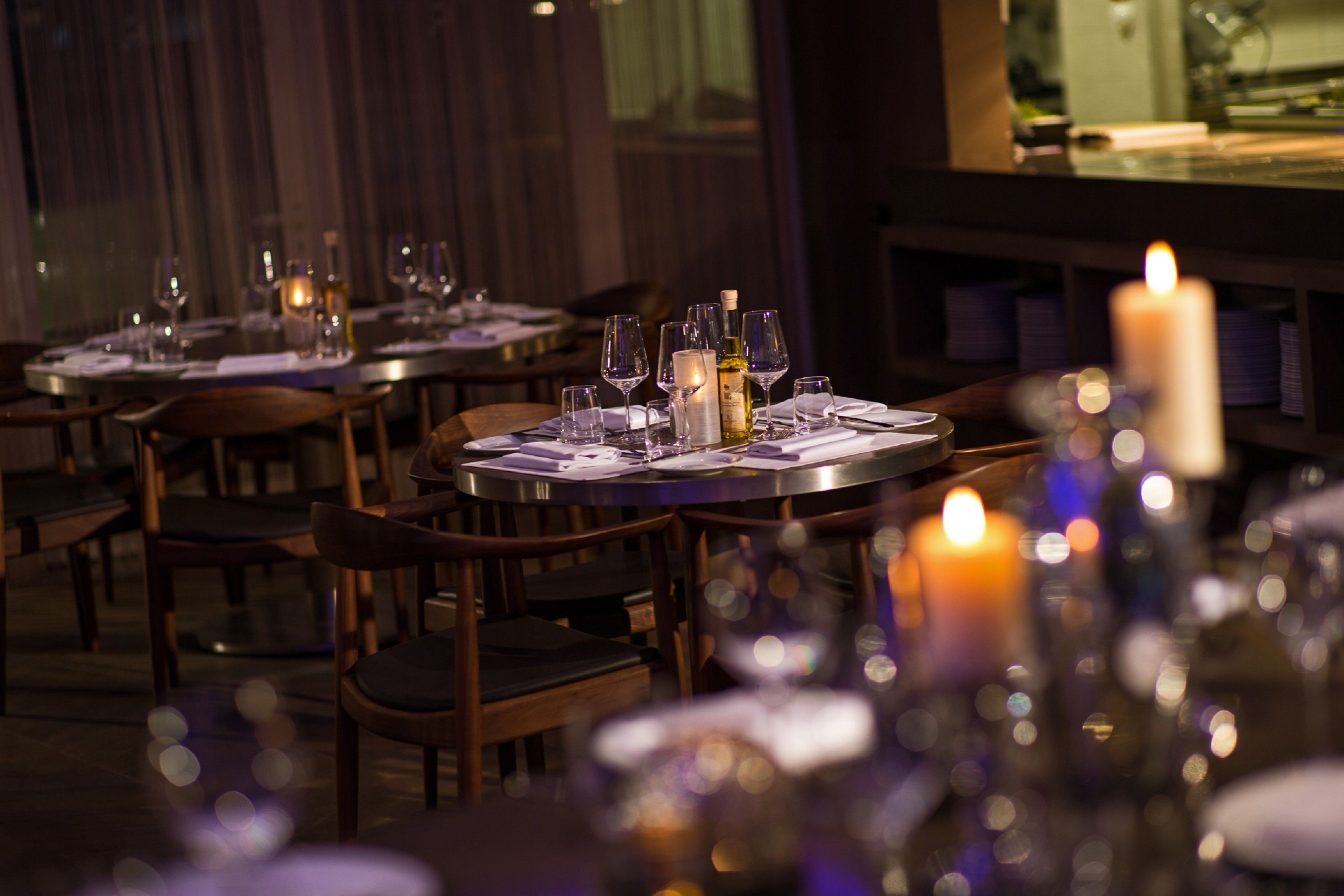 A dimly lit restaurant with round tables set for dining, featuring candles and wine glasses.