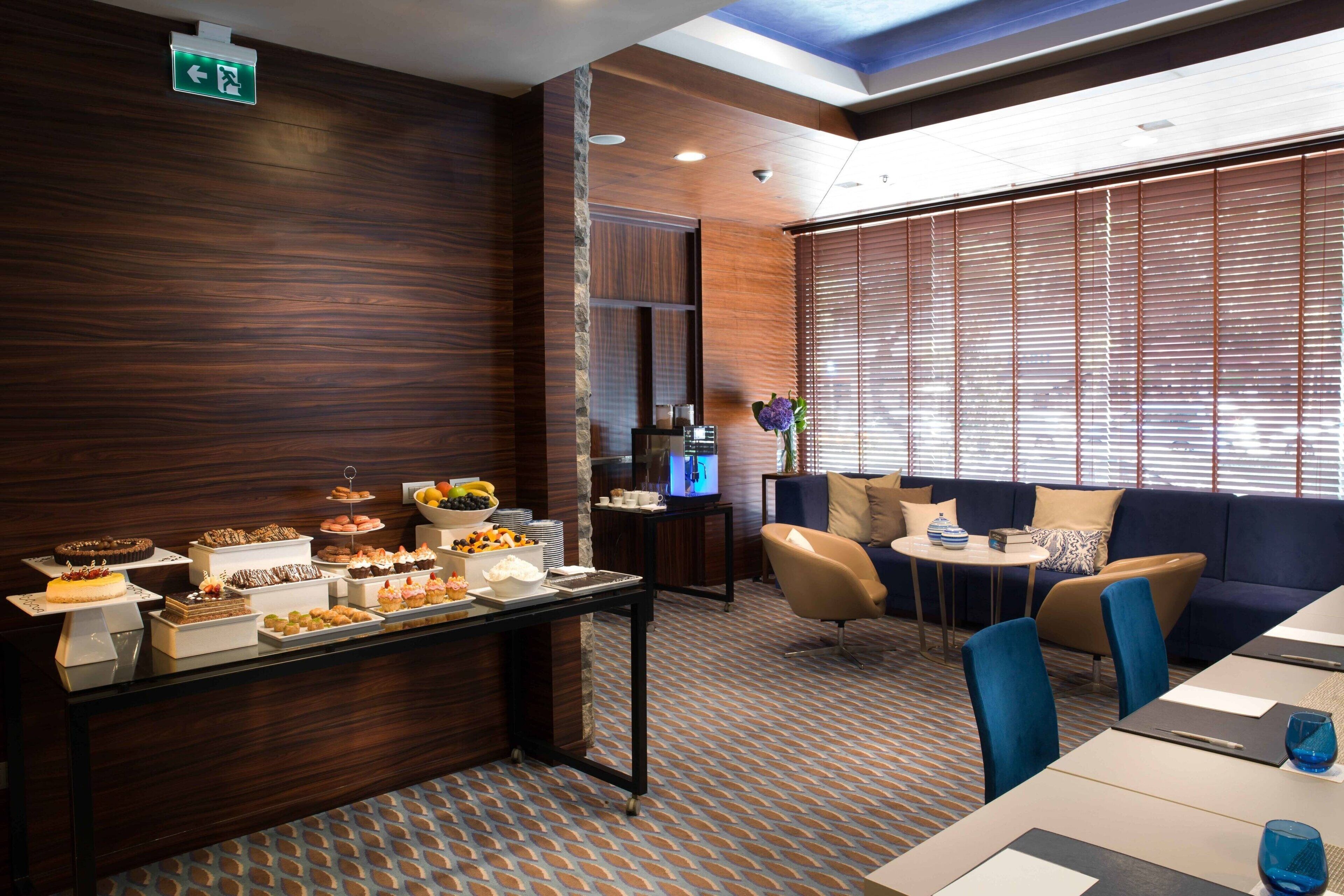 Un vestíbulo de hotel con zona de buffet, asientos y televisión.