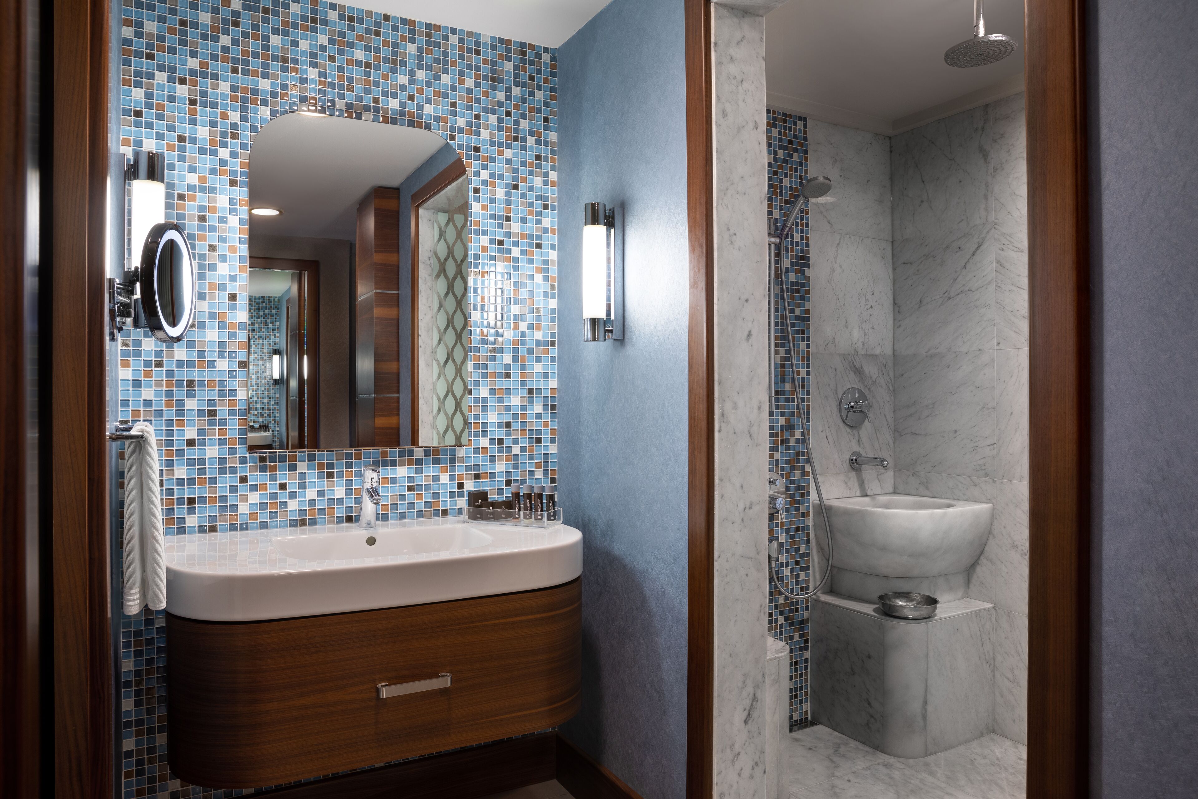 A modern bathroom with a tiled backsplash, a wooden vanity, a large mirror, and a separate sink area.