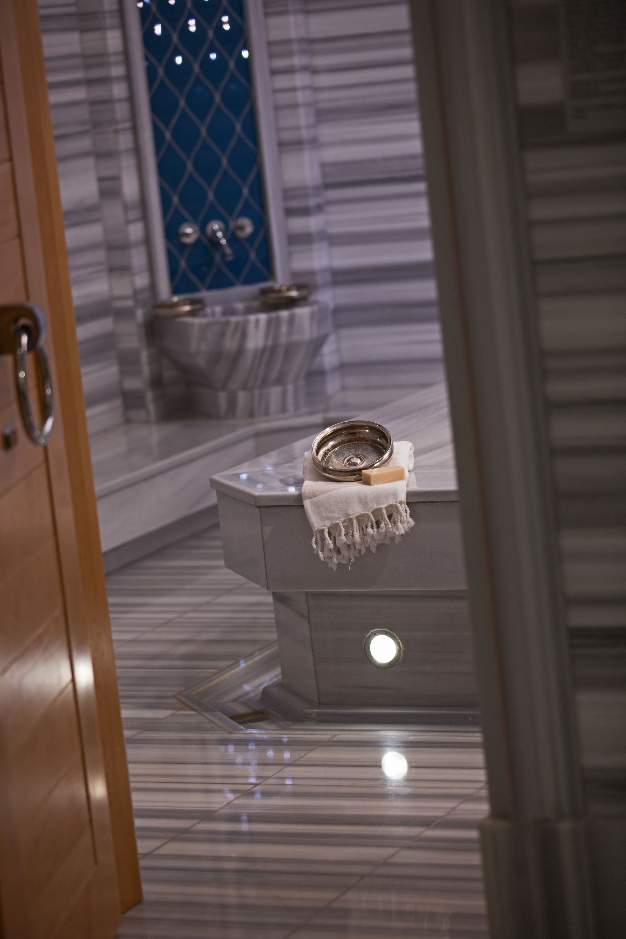 Un baño con suelo de mármol, un lavabo con jabonera y una toalla colgada en el perchero.