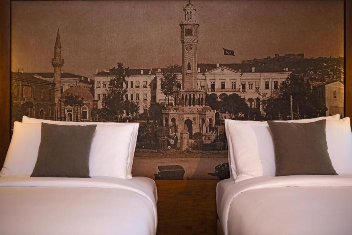 A hotel room with two beds, a large wall tapestry depicting a historical building, and a flag above the tapestry.