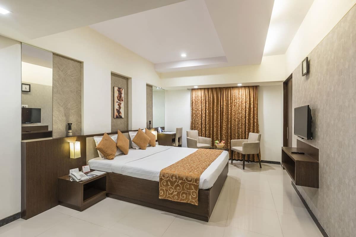A hotel room with a large bed, bedside tables, a desk, a chair, a TV, and curtains.
