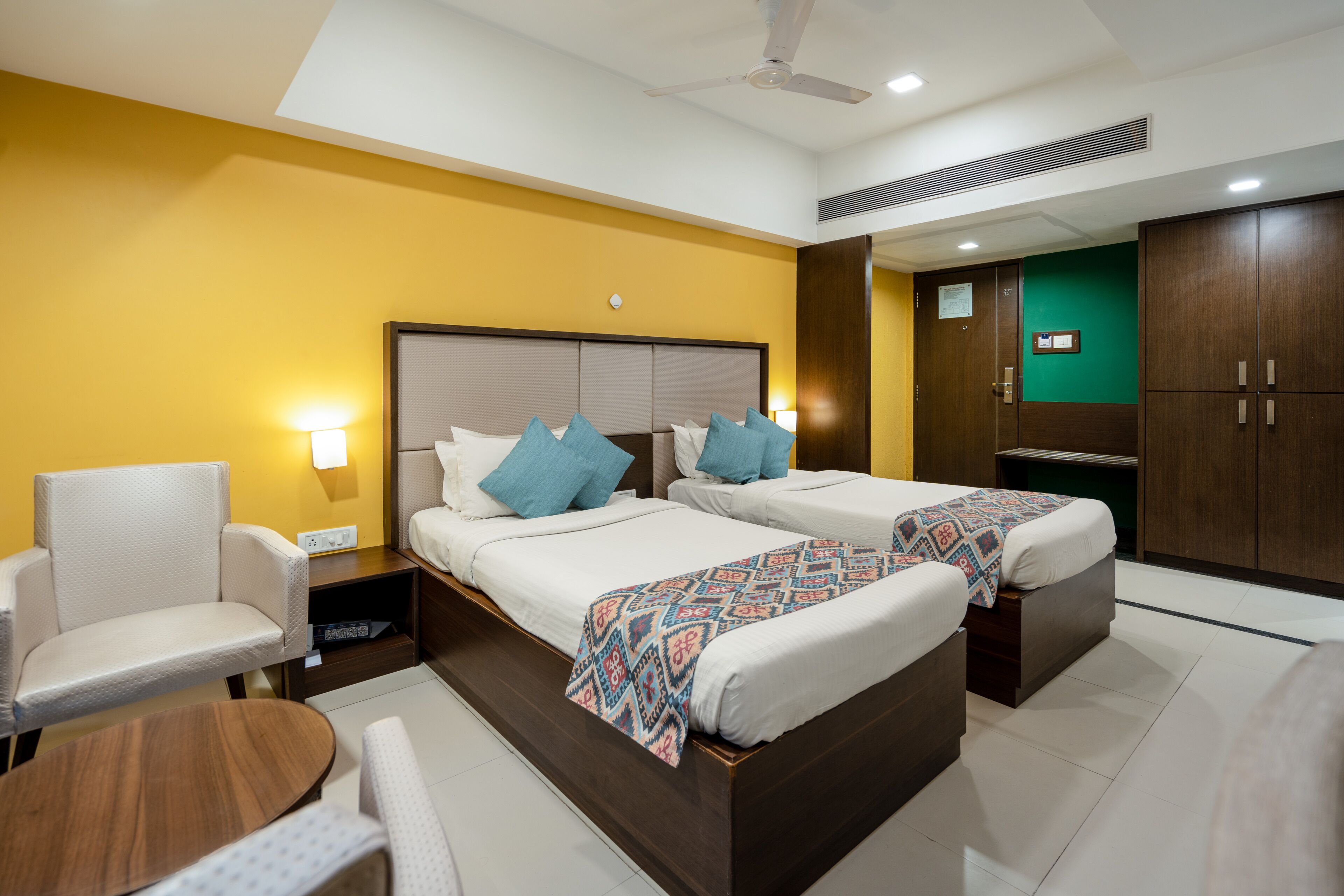 A hotel room with two beds, a sofa, a small table, and a wardrobe.