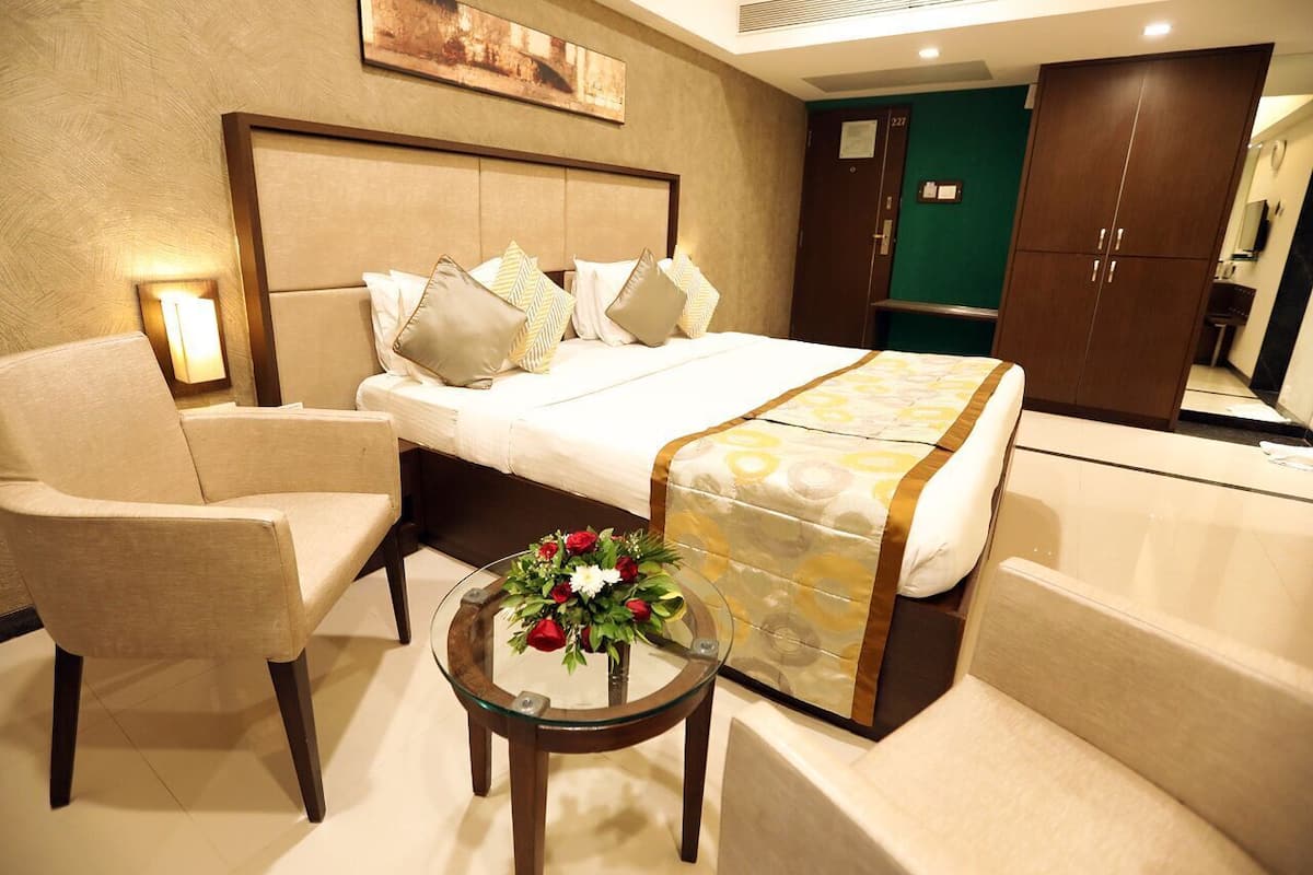 A hotel room with a bed, two armchairs, a small table with a flower arrangement, and a mirror.