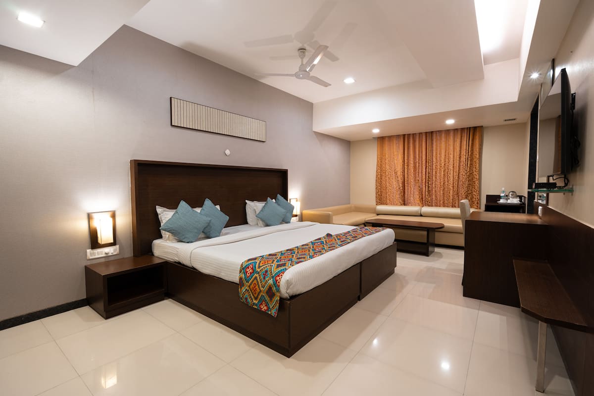 A modern hotel room with a large bed, a desk, a sofa, and a ceiling fan.