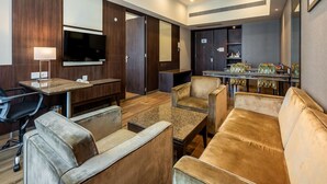 A modern hotel room with a sofa, armchairs, a desk, a television, and a dining area. - GCC Hotel and Club (Mumbai)