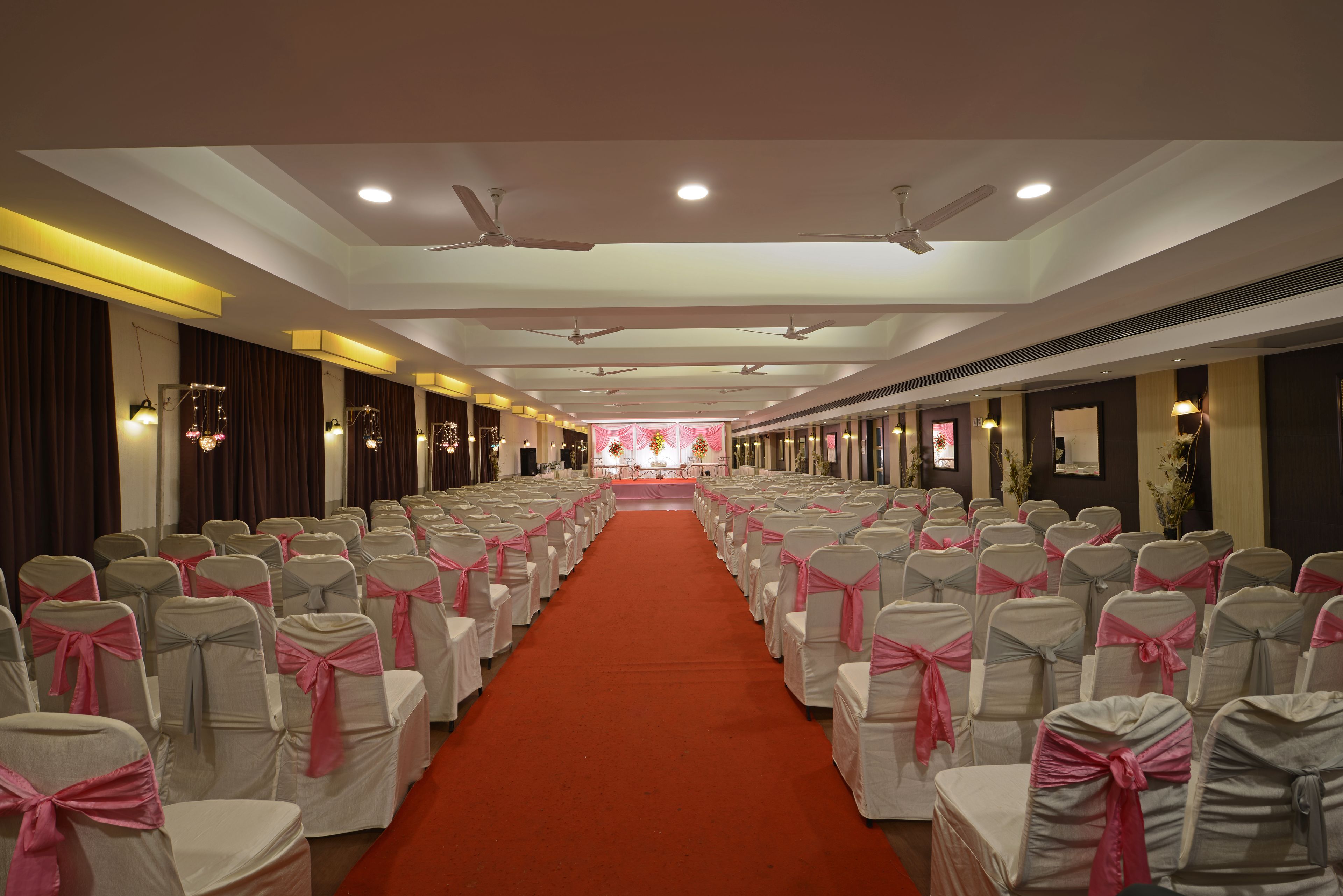 Un salón de conferencias de hotel con filas de sillas, una alfombra roja, ventiladores de techo e iluminación empotrada.