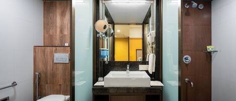 Un baño moderno con inodoro blanco, lavamanos con espejo y zona de ducha.