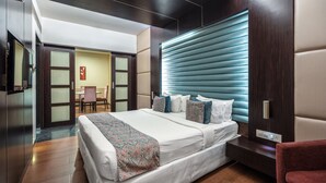 A modern hotel room with a large bed, a seating area, and a view of the hallway. - GCC Hotel and Club (Mumbai)