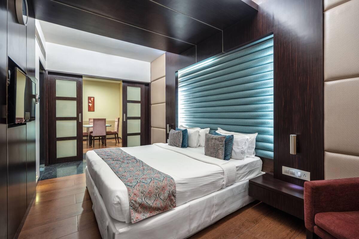 A modern hotel room with a large bed, a seating area, and a view of the hallway.