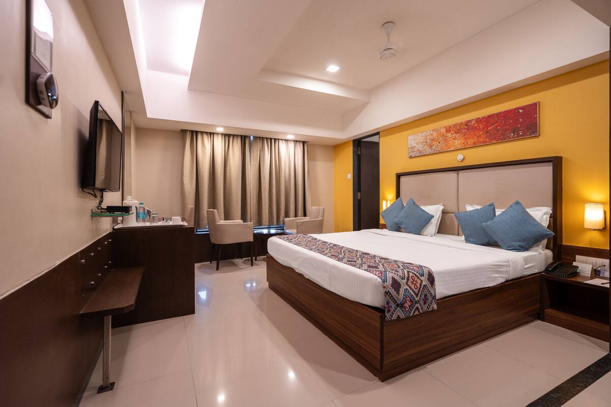 A modern hotel room with a large bed, a desk, a chair, and a television.