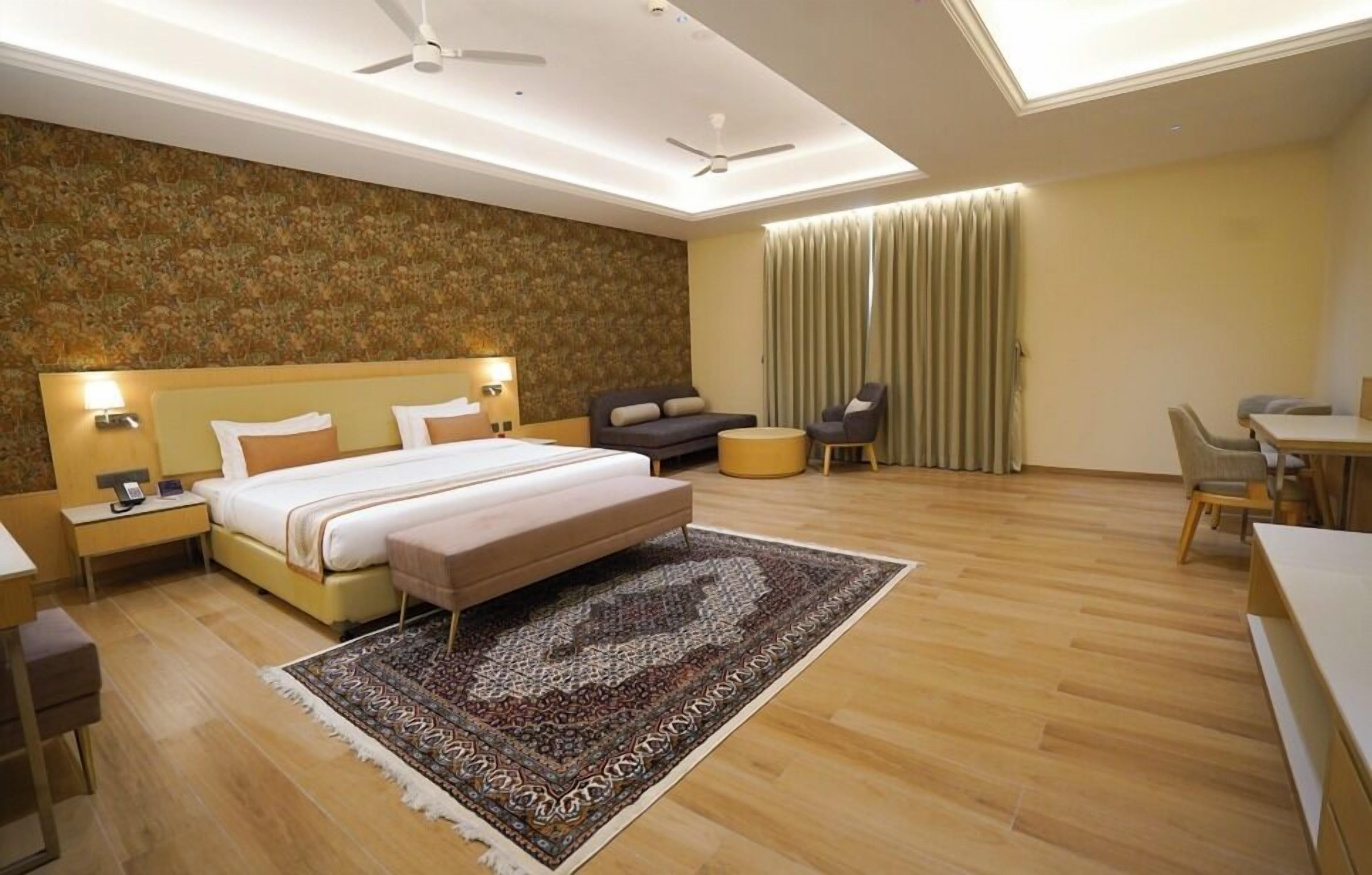 A modern hotel room with a large bed, bedside tables, a sofa, a desk, and a chair.