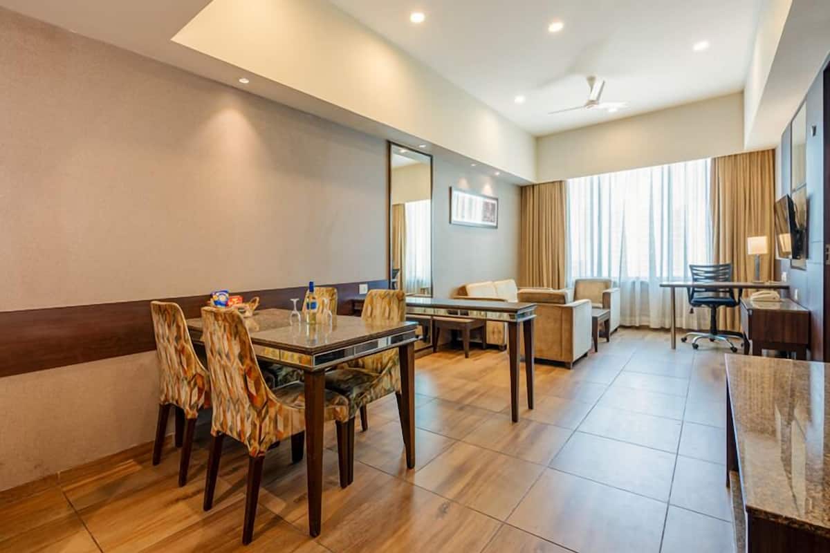 A hotel room with a dining area, a sofa, a TV, and a desk.
