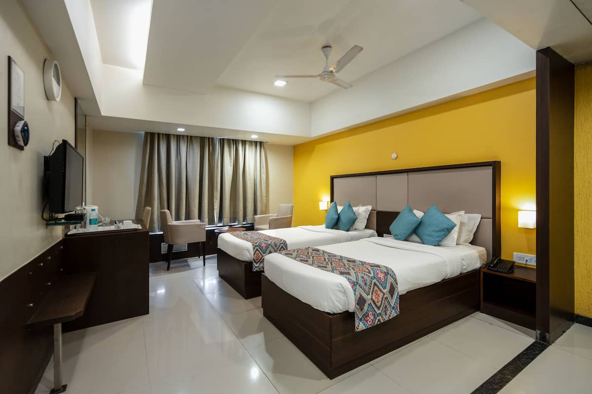 A hotel room with two beds, a desk, a chair, a TV, and a ceiling fan.