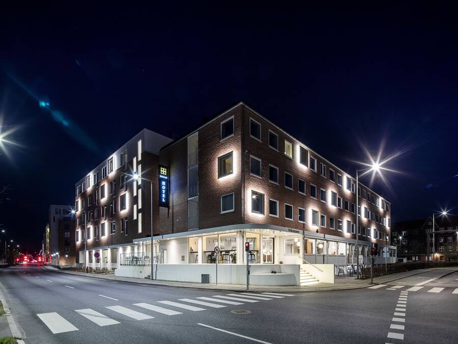 A modern hotel with a glass facade, multiple floors, and a ground-level restaurant.