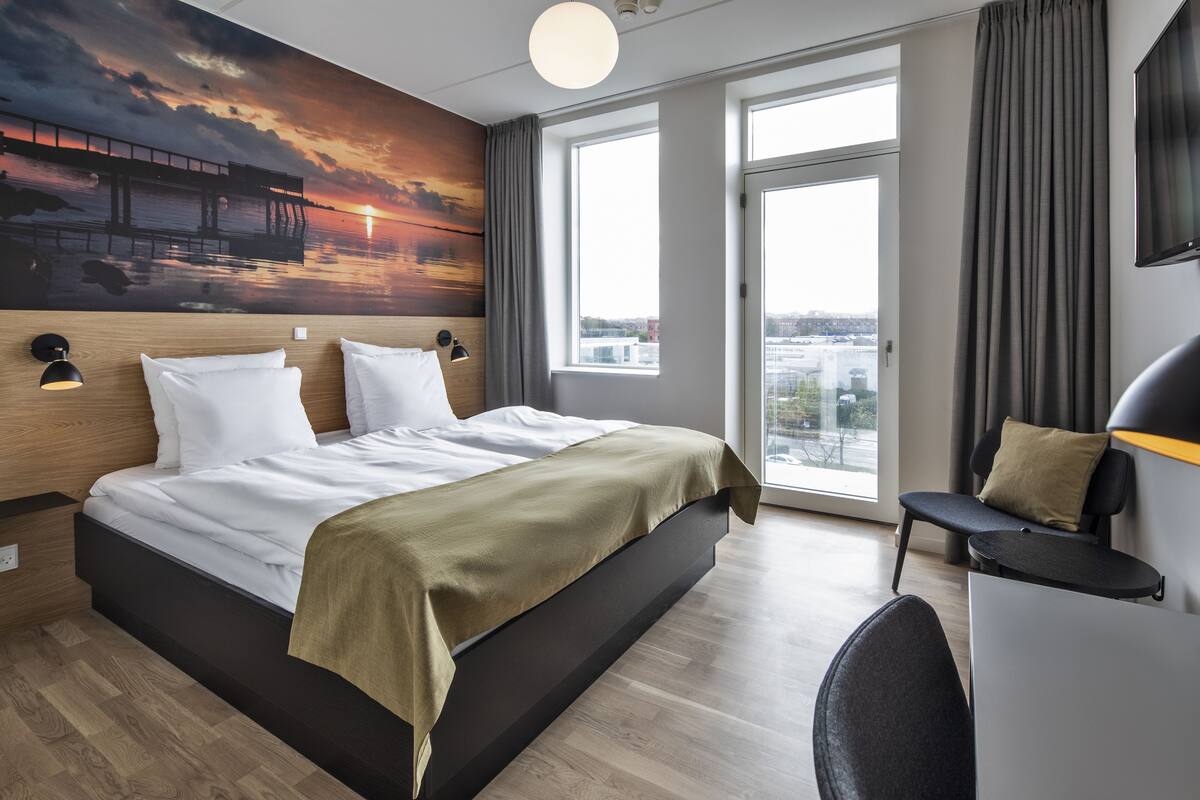 A modern hotel room with a large bed, a desk, and a city view.