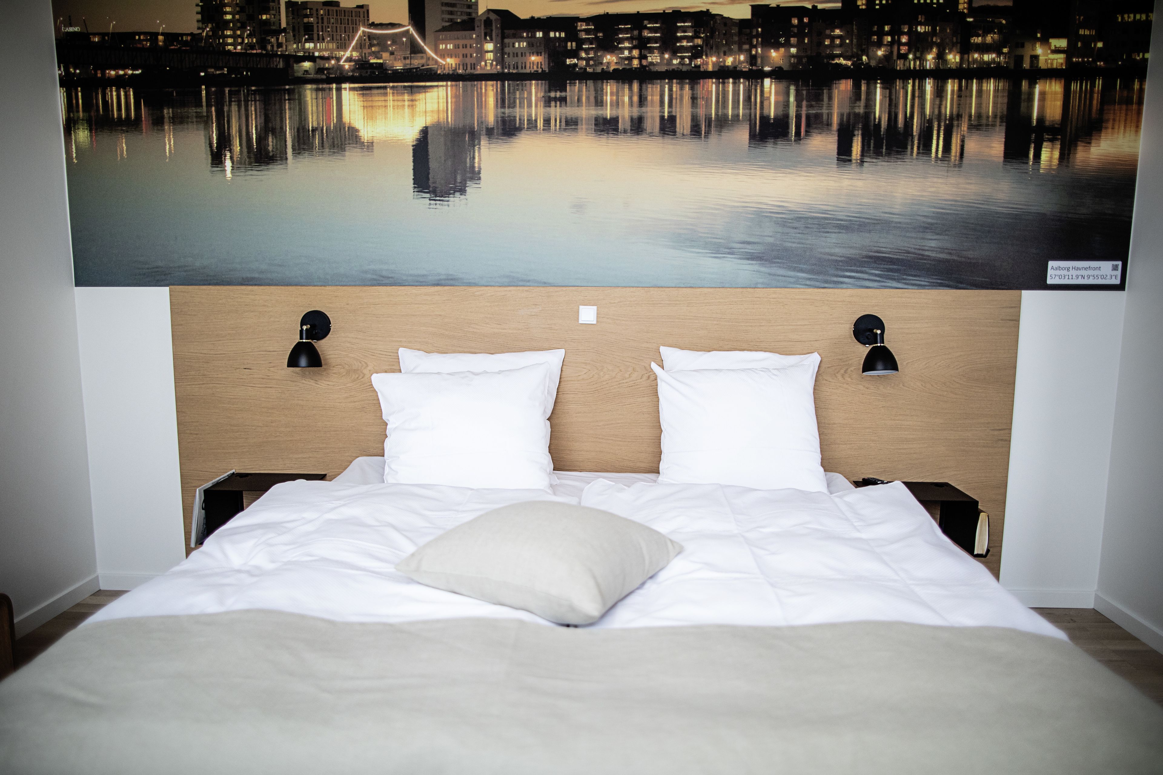 A hotel room with a bed, two bedside lamps, and a cityscape view.