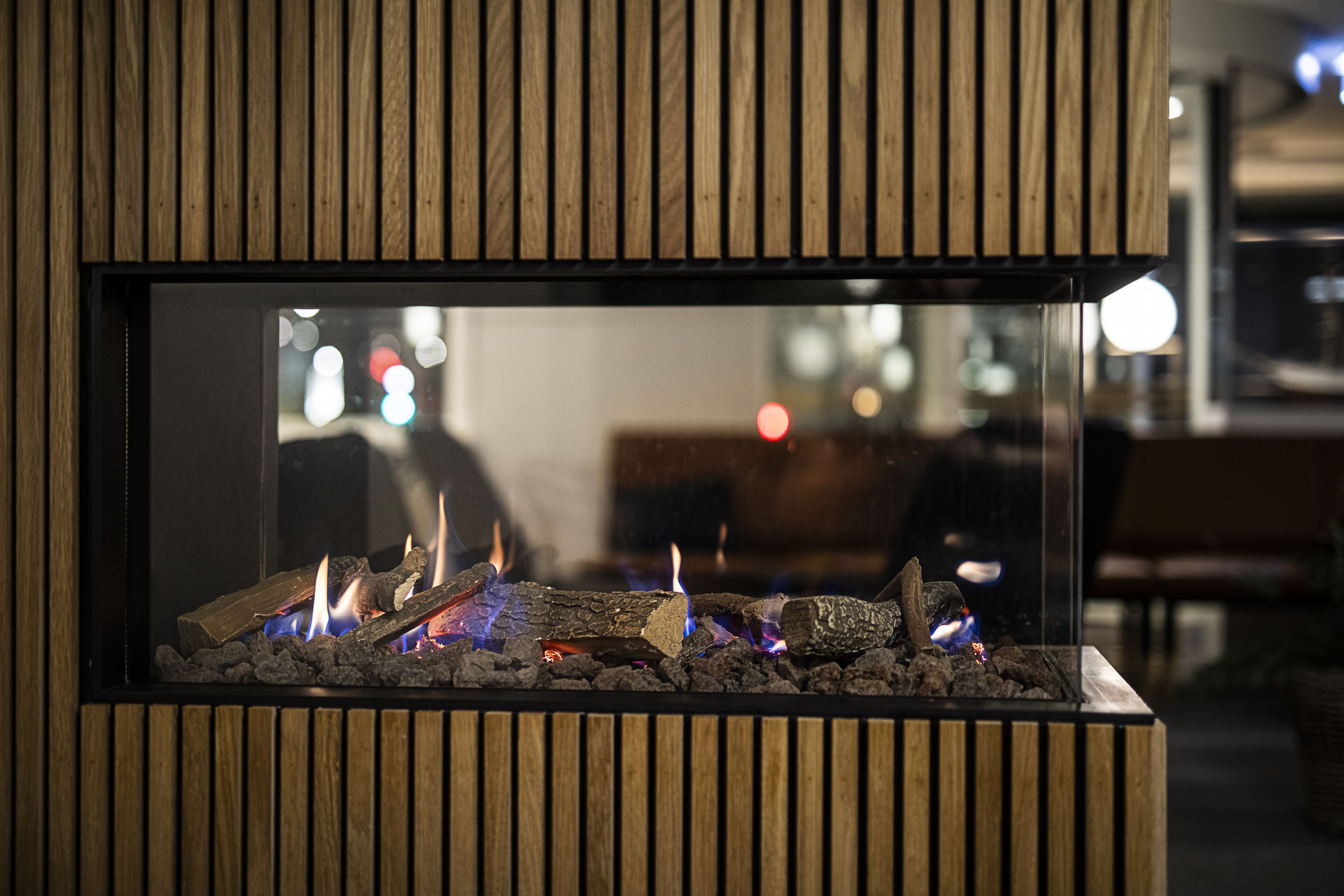 Una chimenea moderna con recinto de vidrio, frente a un panel de madera.