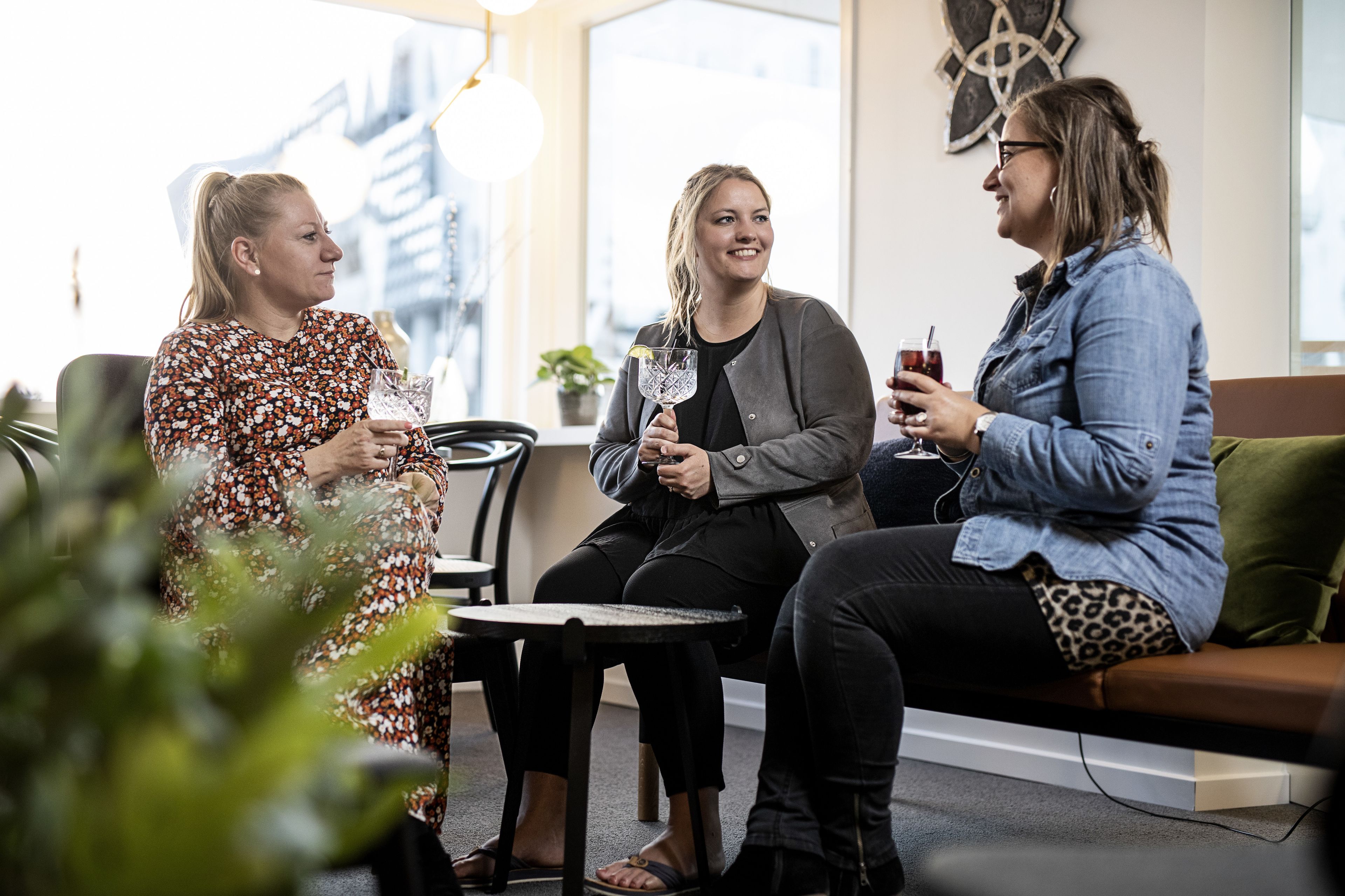 Three people seated on a couch in a well-lit indoor space with a modern design, including a geometric wall art piece and a potted plant.
