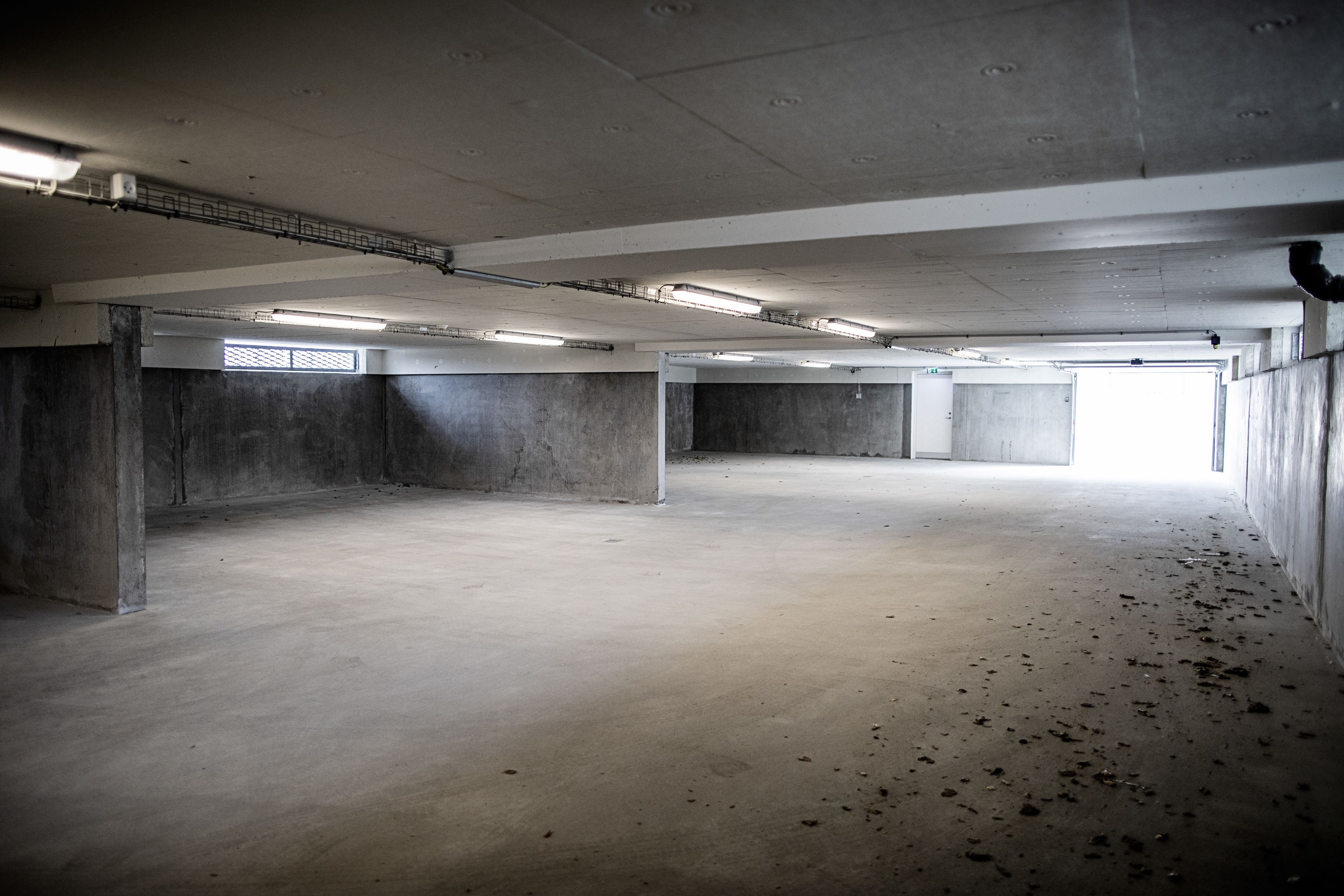 An empty parking garage with concrete walls, a flat floor, and fluorescent lighting.