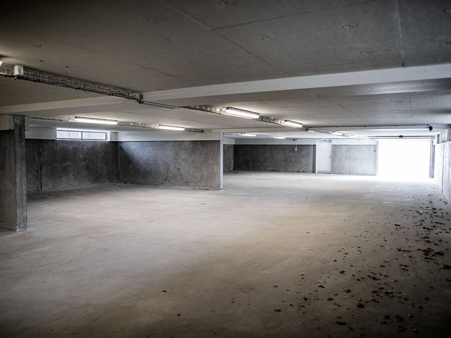 An empty parking garage with concrete walls, a flat floor, and fluorescent lighting.