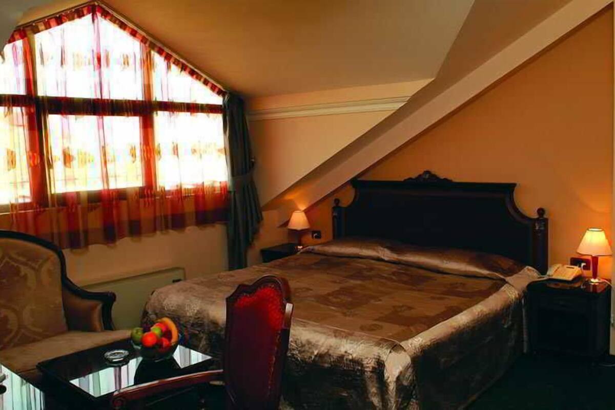 Una habitación de hotel con una cama grande, una silla, una mesita con fruta y una lámpara en la mesita de noche.