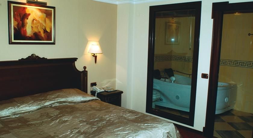 Ein Hotelzimmer mit Bett, Nachttisch, Lampe, einem Gemälde und einem Badezimmer mit Badewanne und Toilette.