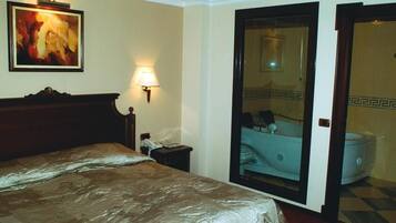 Ein Hotelzimmer mit Bett, Nachttisch, Lampe, einem Gemälde und einem Badezimmer mit Badewanne und Toilette.