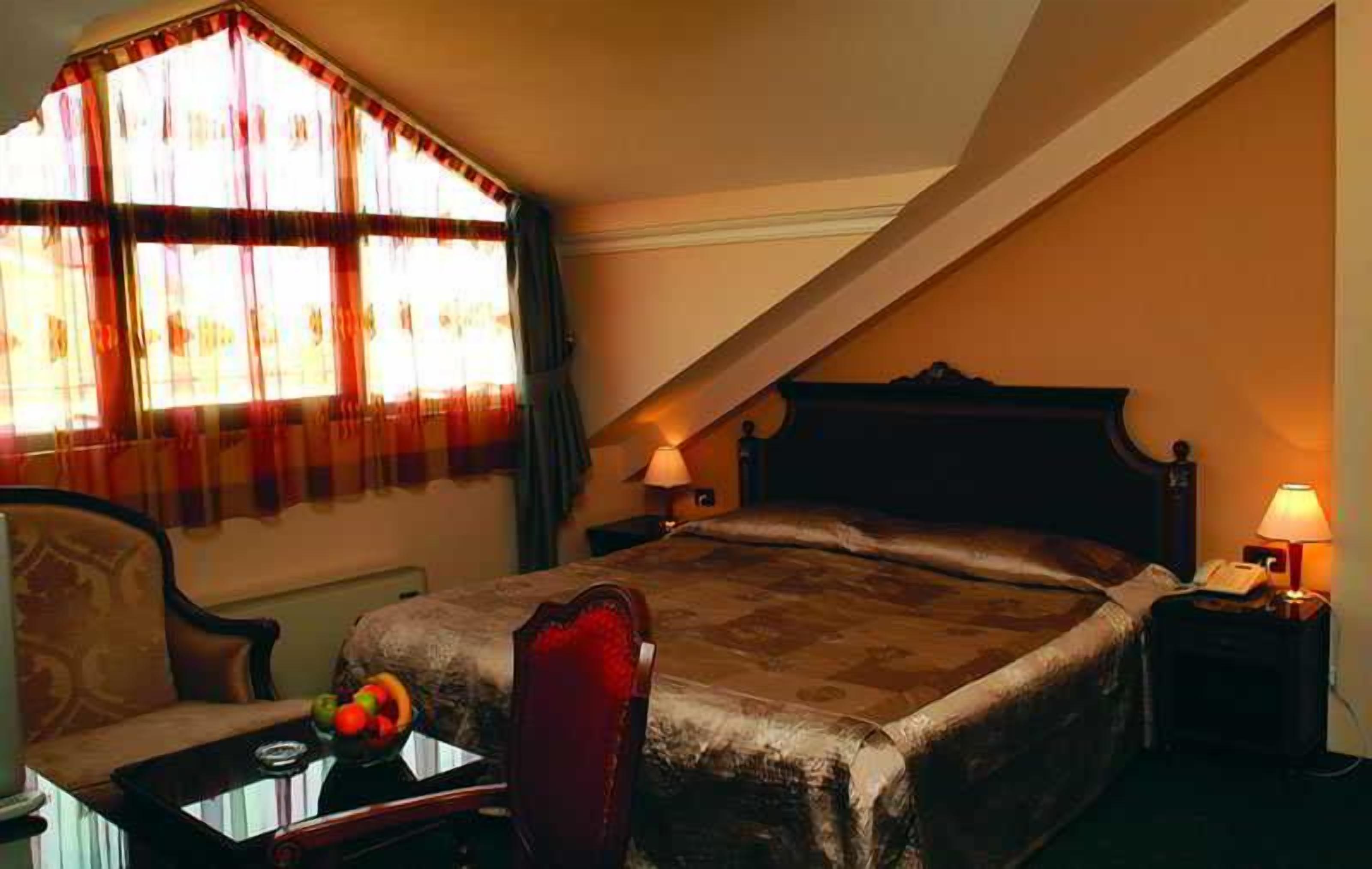 Ein Schlafzimmer mit einem Bett, einem Sessel, einem Nachttisch mit Lampe und einem fensterbepflanzten Fenster.