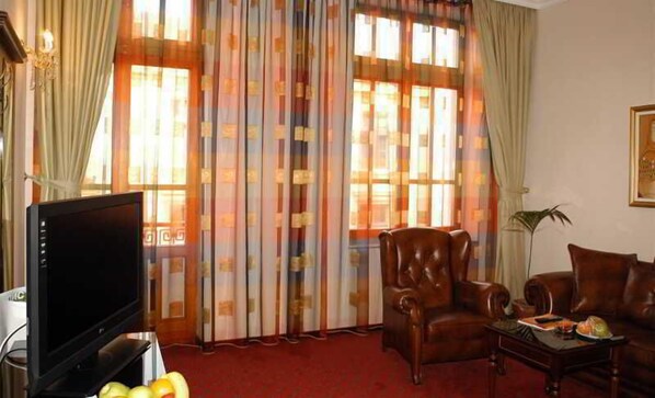 Una sala de estar con televisor, sillones de cuero, una mesita de centro y un amplio ventanal con cortinas.