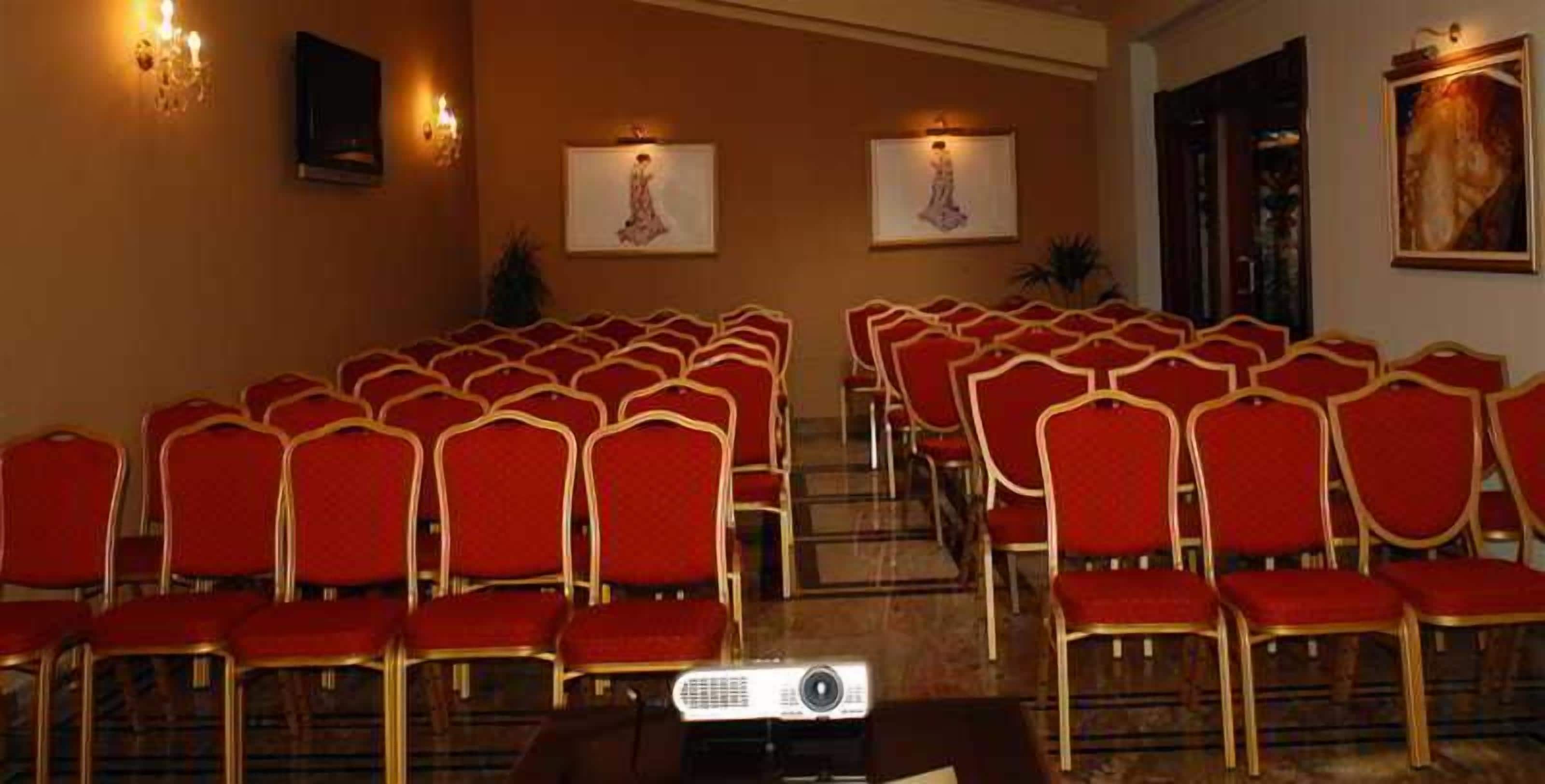 Une salle de conférence avec des rangées de chaises rouges et un écran de projection.