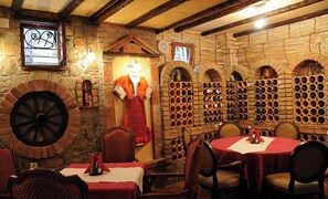 A rustic interior with stone walls, a large wine rack, and a round table with chairs. - Millenium Palace Bitola (Bitola)