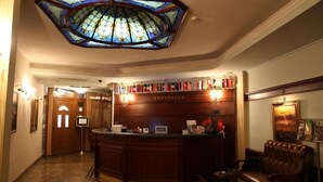 A reception desk with a 'RECEPTION' sign, a stained glass ceiling, a leather chair, and a framed picture on the wall. - Millenium Palace Bitola (Bitola)