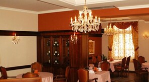 Un espace repas avec des tables rondes, des chaises, des lustres et une grande fenêtre agrémentée de rideaux.