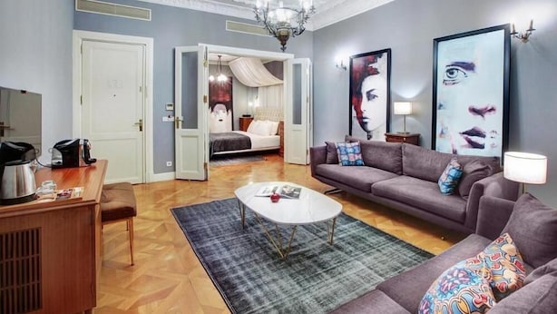Una sala de estar moderna con un sofá, una mesa de centro y obras de arte. Se ve una cama al fondo.