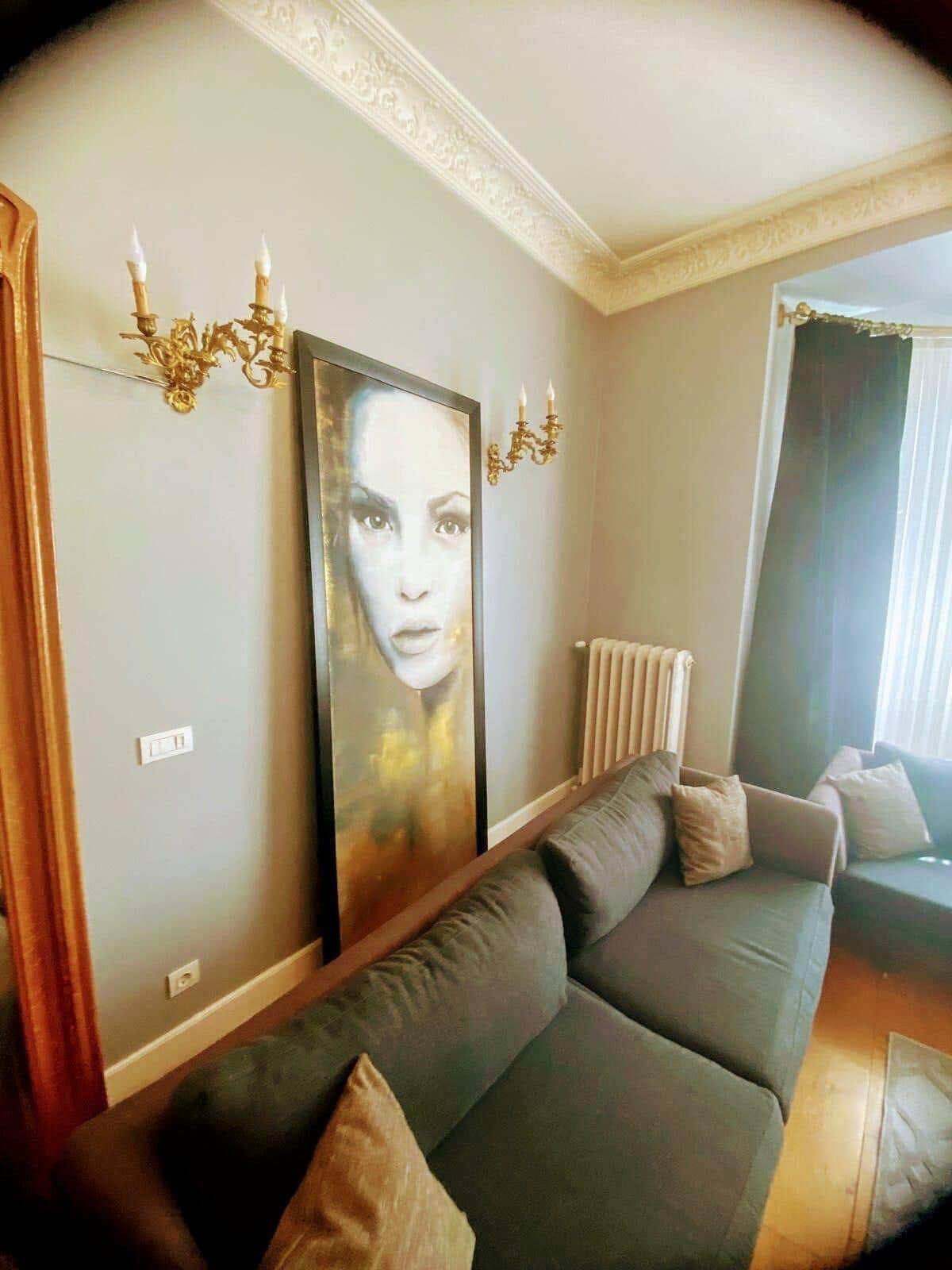 A living room with a grey sofa, two wall-mounted chandeliers, and a large framed artwork.