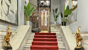 Una imponente escalera con alfombra roja, flanqueada por estatuas doradas de caballos, que conduce a un salón con un espejo grande y una araña.