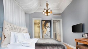Un dormitorio con cabecera capitonada, un televisor de pantalla plana, una mesita de noche y un cuadro grande en la pared.