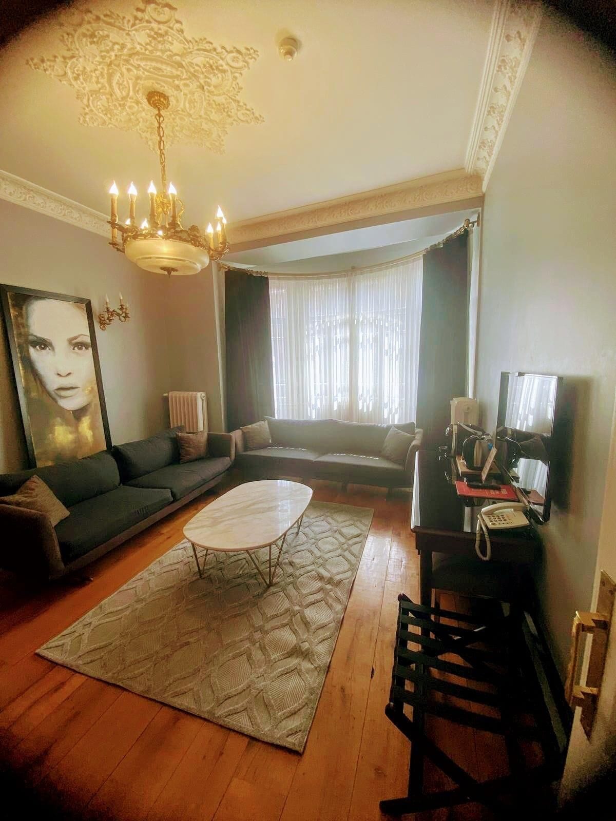 A living room with a sofa, a coffee table, a chandelier, a television, and a telephone.