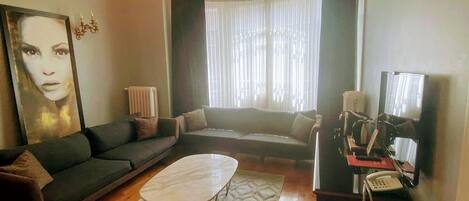 A living room with a sofa, a coffee table, a chandelier, a television, and a telephone.
