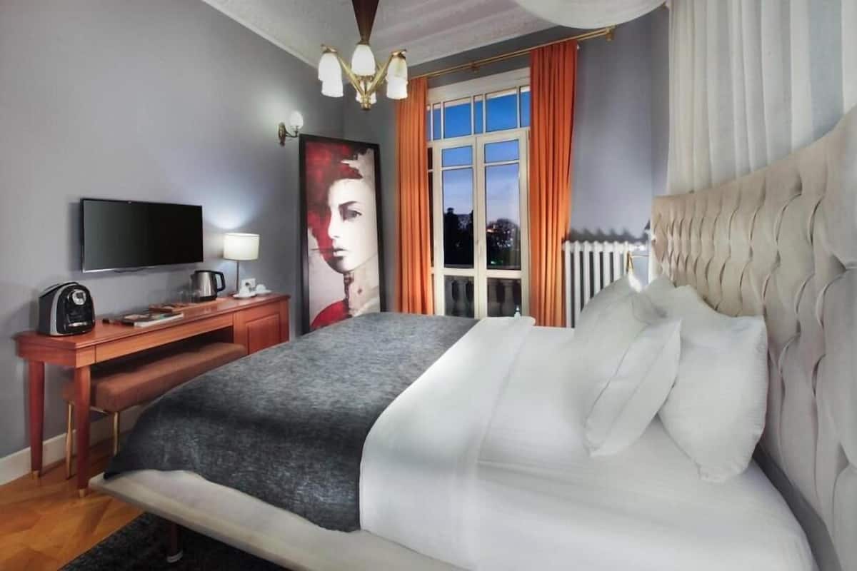 Un dormitorio con una cama grande, televisión de pantalla plana, escritorio con lámpara y ventana con cortinas.
