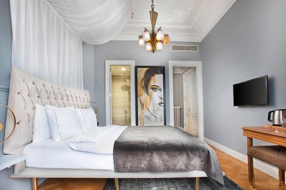 Un dormitorio con cabecera capitonada, un televisor de pantalla plana, una mesita de noche y un cuadro grande en la pared.
