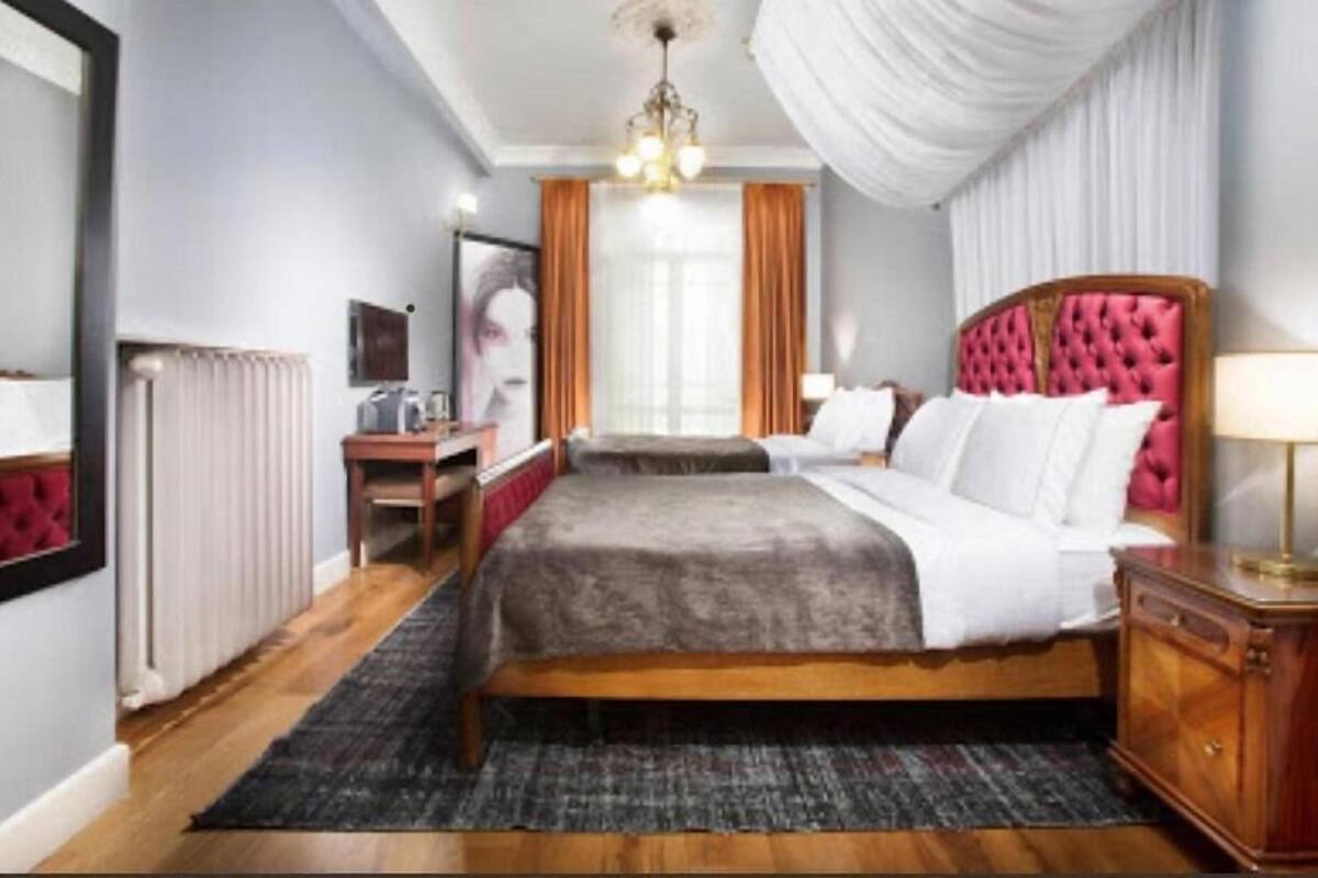 Habitación de hotel con una cama grande, un aparador de madera, un escritorio con silla, un radiador y una araña.