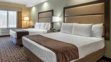 Habitación de hotel con dos camas, un ventanal con cortinas, una lámpara de pie y una alfombra estampada.