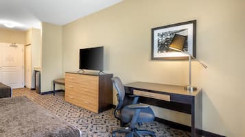 Una habitación de hotel con cama, escritorio, silla, televisión, lámpara y un cuadro en la pared.