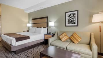A hotel room with a bed, a sofa, a nightstand, a lamp, and a framed picture on the wall.