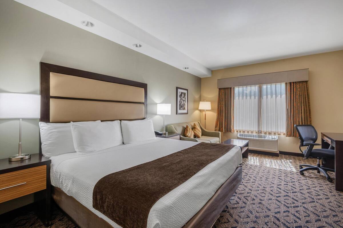 Een hotelkamer met een groot bed, een bureau, een stoel, een bank en een raam met gordijnen.
